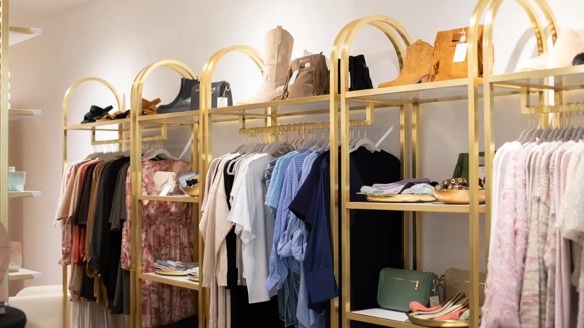 Goldener metallischer Kleiderständer mit gewölbten Regalen und hängender Kleidung