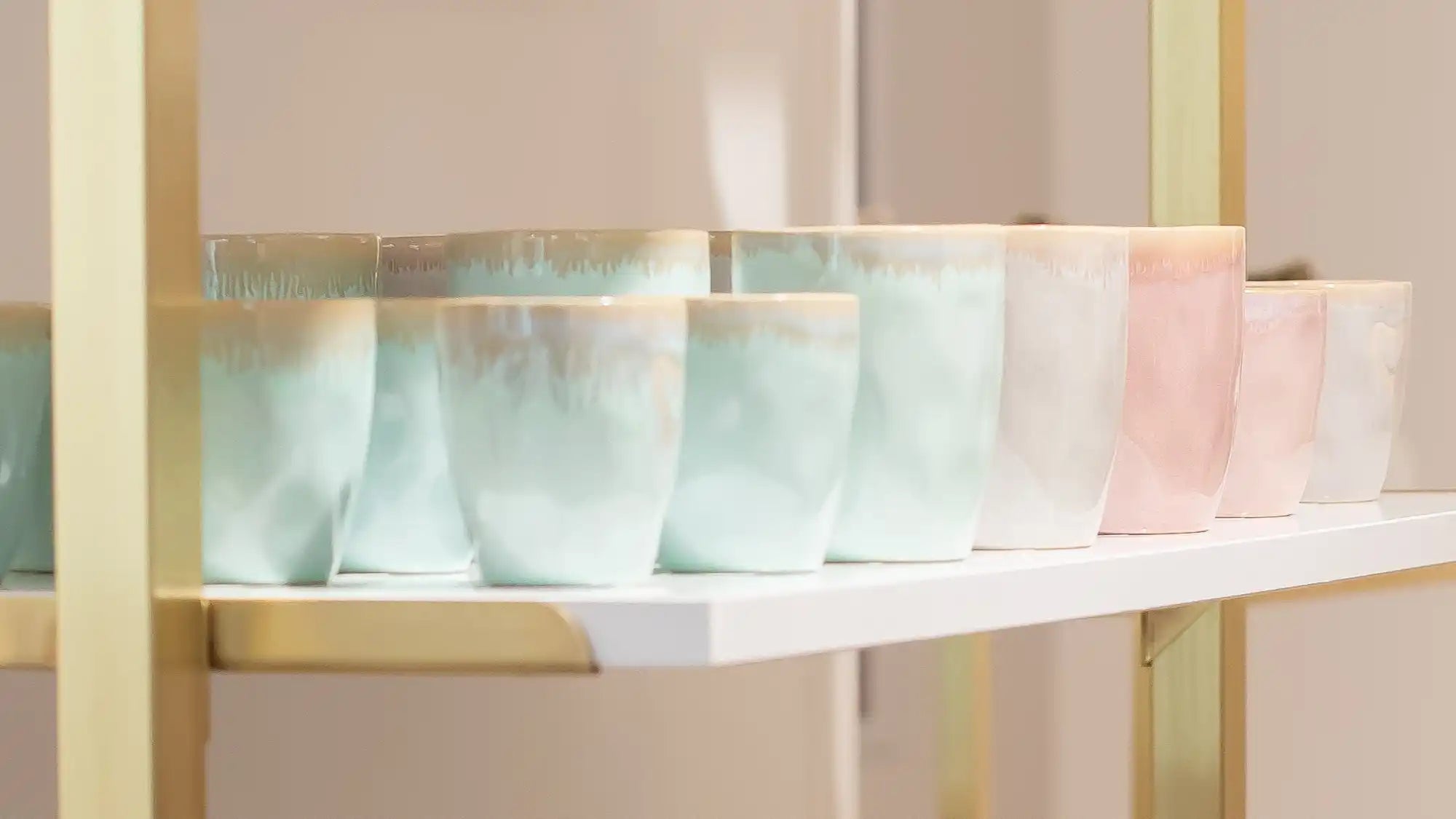 Pastellfarbene Keramikbecher auf einem weißen Regal mit goldenen Akzenten.